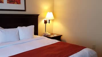 Una cama bien hecha con ropa de cama blanca y roja, una lámpara de noche y un cuadro en la pared.