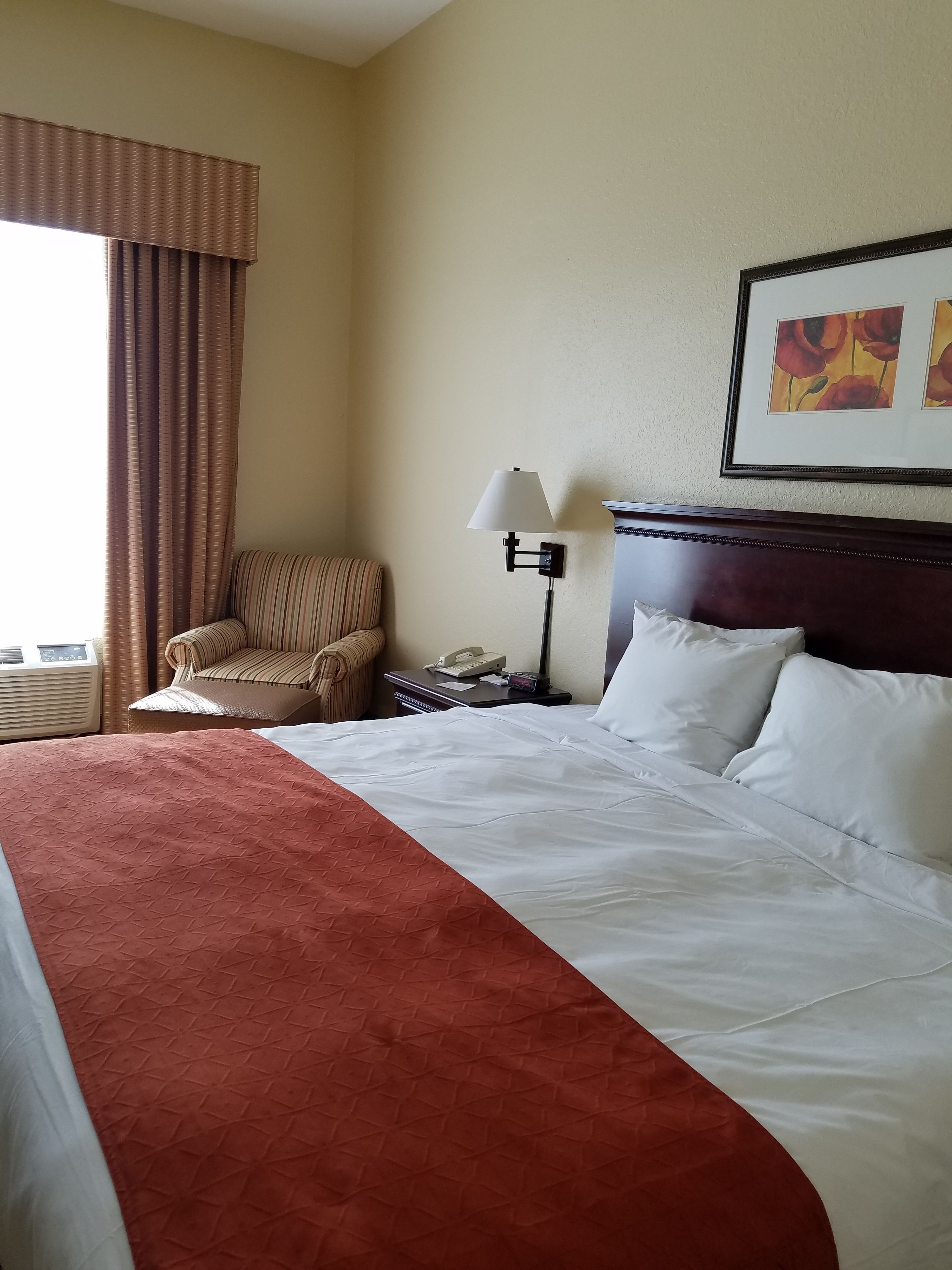 A hotel room with a large bed, a chair, a bedside table with a lamp, and a painting on the wall.