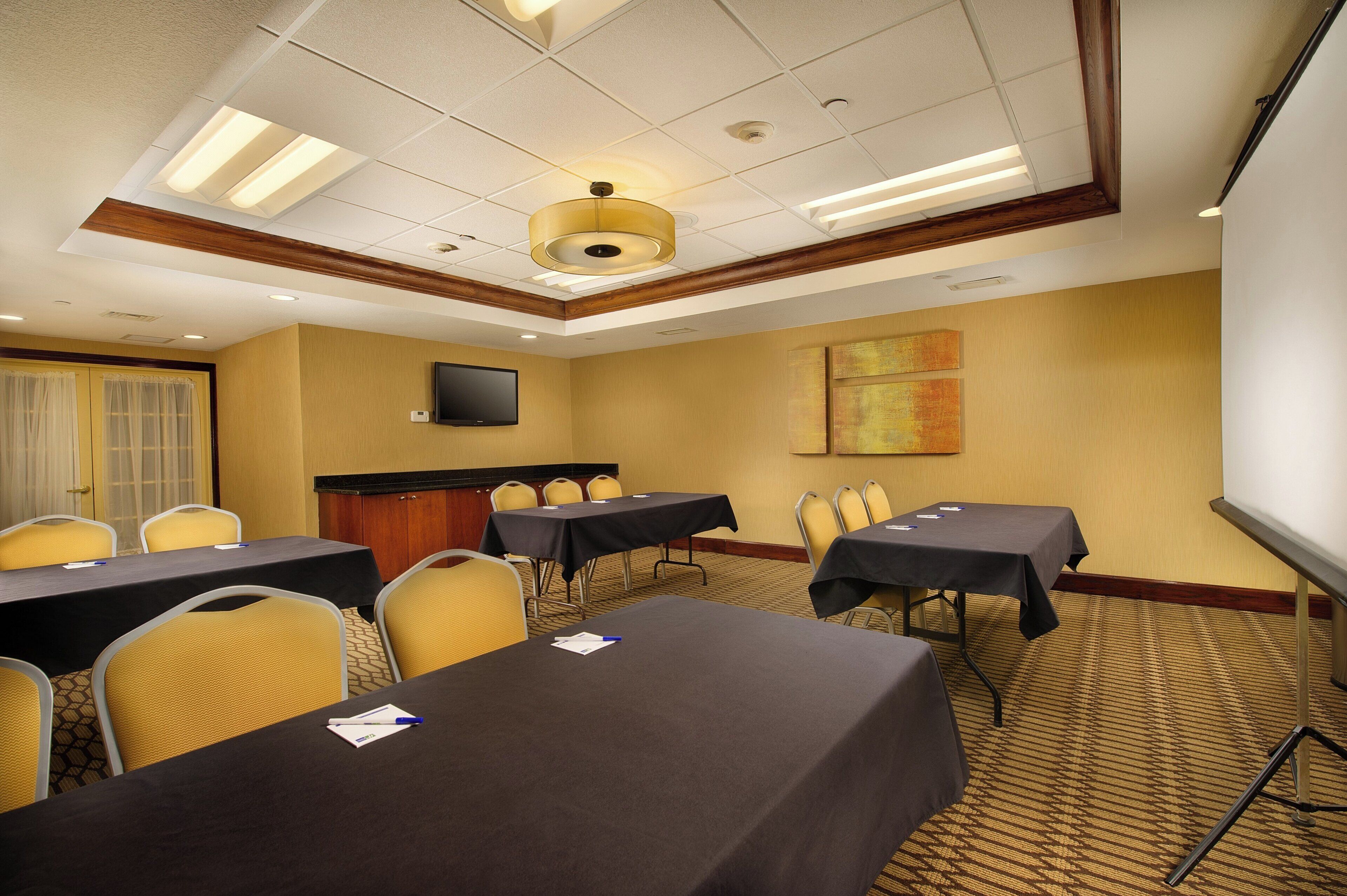 Un salón de conferencias con mesas, sillas, una pantalla de proyector y una televisión.