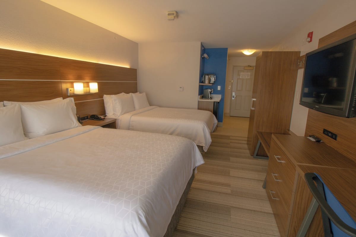 Een hotelkamer met twee bedden, een bureau met een televisie, een kleine kitchenette en een badkamer op de achtergrond.