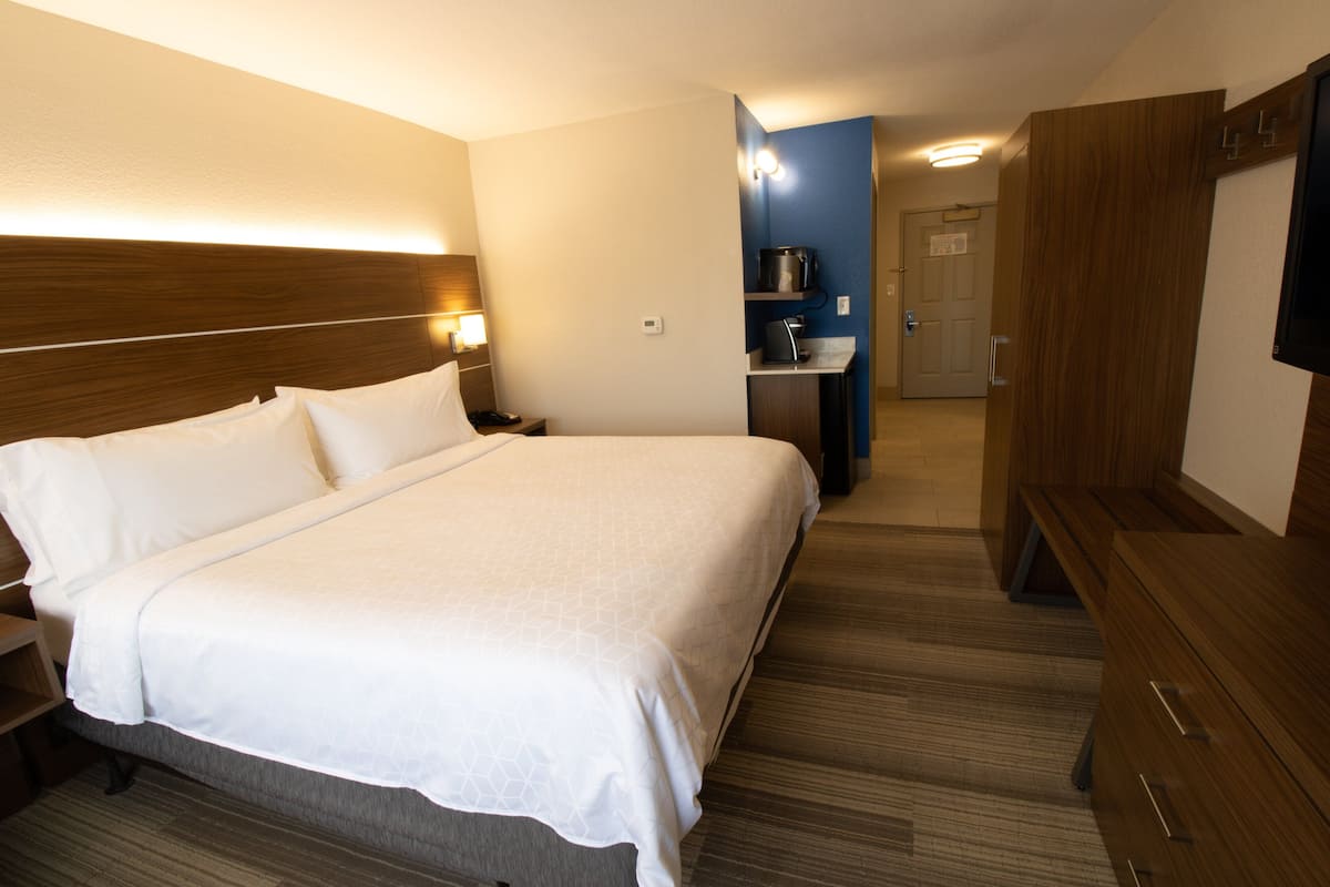 Hotellihuone, jossa on suuri sänky, yöpöydät, taulutelevisio, työpöytä tuolilla ja vaatekaappi.