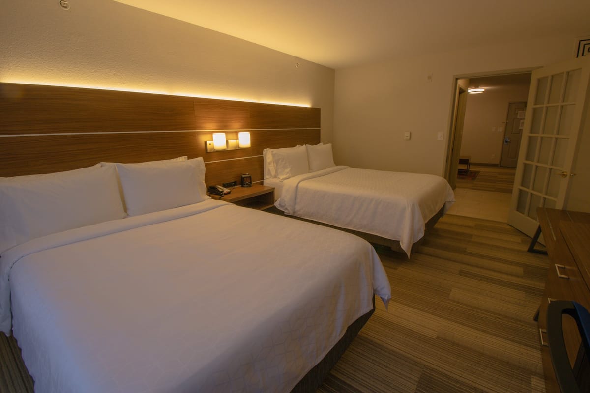 Hotellihuone, jossa on kaksi sänkyä, puinen pääty, yöpöytävalaisimet ja puinen työpöytä.