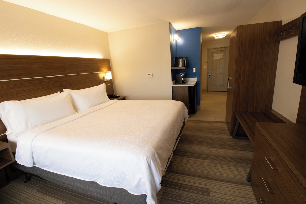 Habitación de hotel con una cama grande, mesitas de noche, un escritorio con silla, televisor y armario.