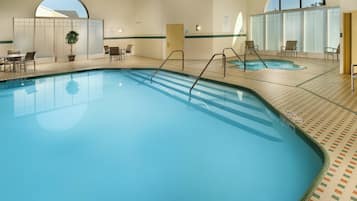An indoor swimming pool with clear water, surrounded by lounge chairs and a small table.