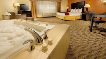 A hotel room with a large bathtub, a bed, a desk, and a television.