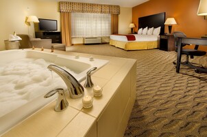 Habitación de hotel con una bañera grande, una cama, un escritorio y un televisor.
