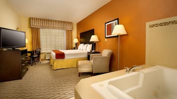 Quarto de hotel com cama, escrivaninha, cadeira, televisão, abajur e banheira.