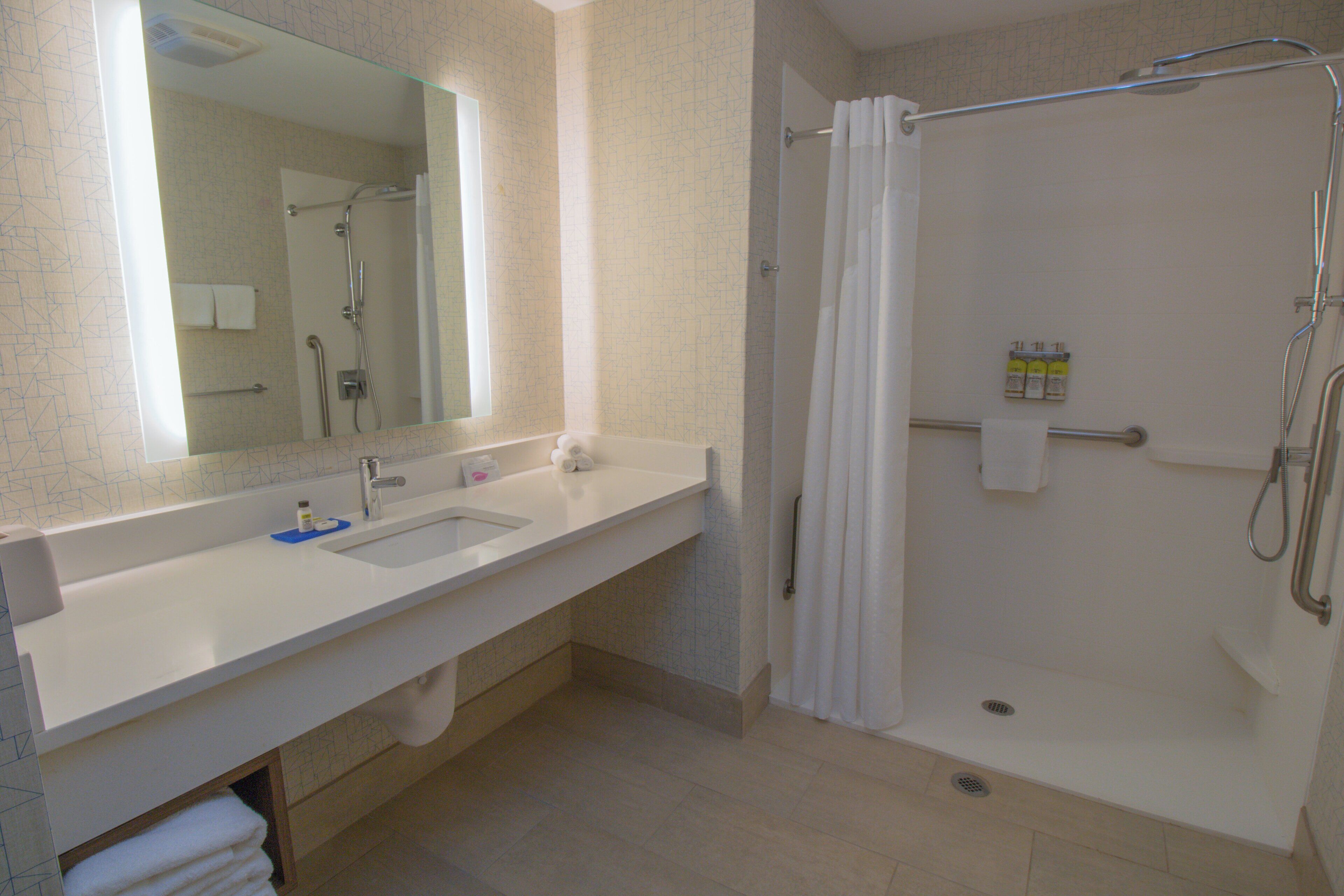 Une salle de bain équipée d’un lavabo, d’un miroir, d’une douche et d’un porte-serviettes.
