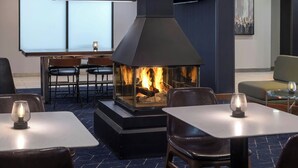 A modern indoor seating area with a fireplace, tables, and chairs. - Courtyard by Marriott Burlington Williston (Williston)