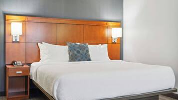 A hotel room with a large bed, wooden headboard, two bedside lamps, a nightstand, and a telephone.