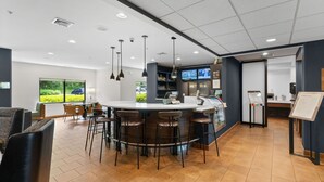 A modern bar area with a central island, bar stools, and a seating area with chairs. - Courtyard by Marriott Burlington Williston (Williston)