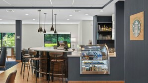 A modern bar area with a central island, bar stools, a refrigerated display case, pendant lighting, and a Starbucks logo on the wall. - Courtyard by Marriott Burlington Williston (Williston)
