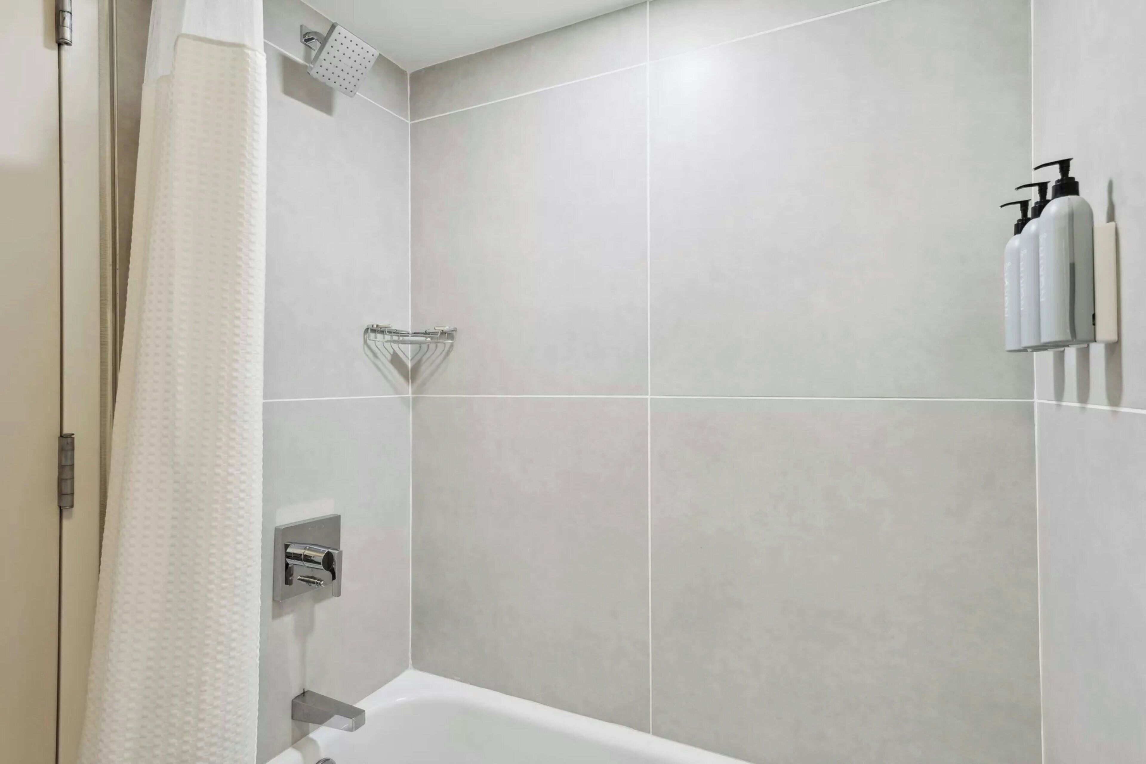 Een moderne badkamer met een badkuip, een douchekop en twee shampoo flessen aan de muur.