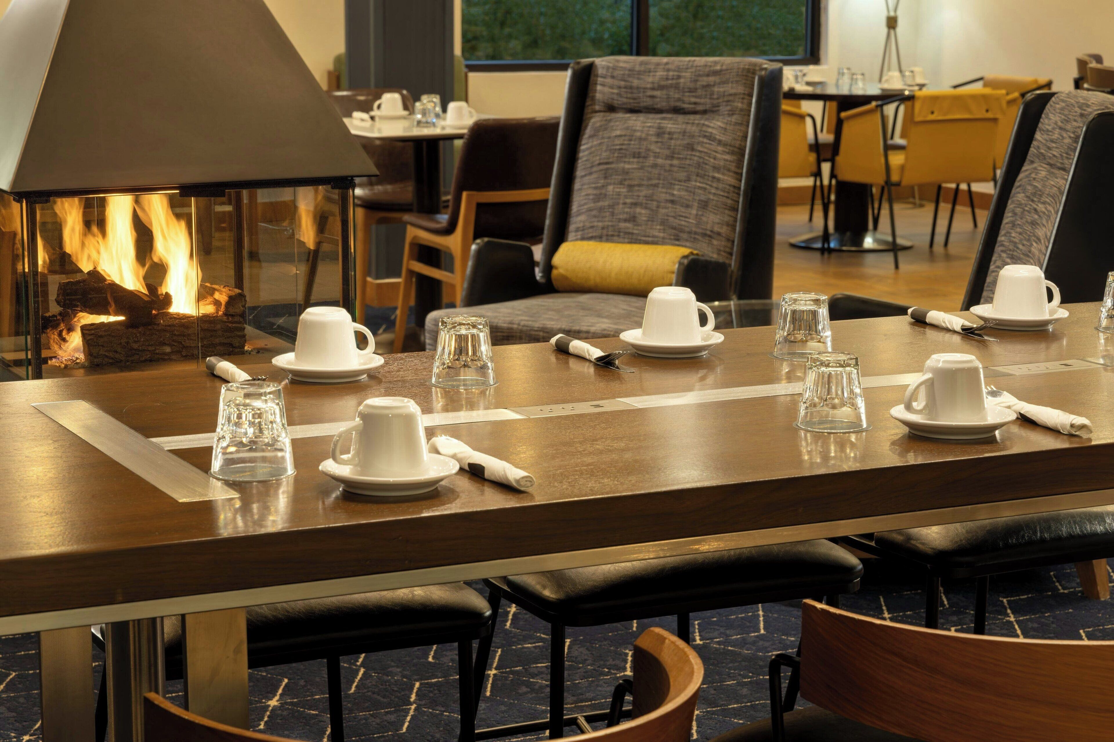 A dining area with a long table set for a meal, a fireplace, and modern furniture.