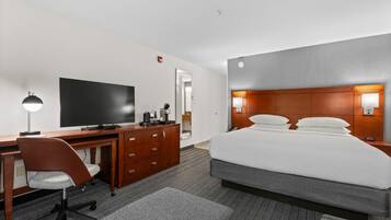 A hotel room with a large bed, a desk with a computer, a chair, and a television.