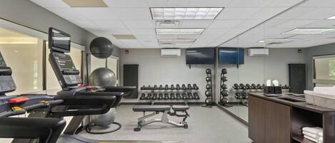 Ein Fitnessstudio mit Laufbändern, Trainingsbällen, Kurzhanteln und einem Fernseher.