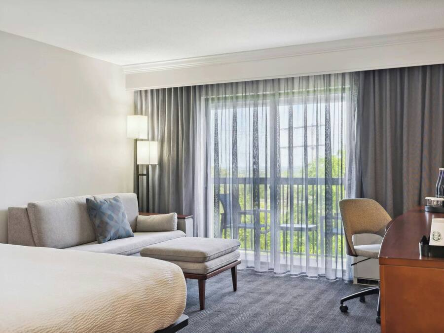 A hotel room with a bed, a sofa, a desk, and a view of the outdoors.