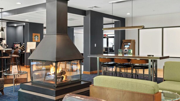 A modern lobby with a central fireplace, seating area, and an ATM machine. - Courtyard by Marriott Burlington Williston (Williston)
