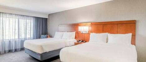 Une chambre d’hôtel avec deux lits, une tête de lit en bois, un téléphone et une fenêtre avec des rideaux.