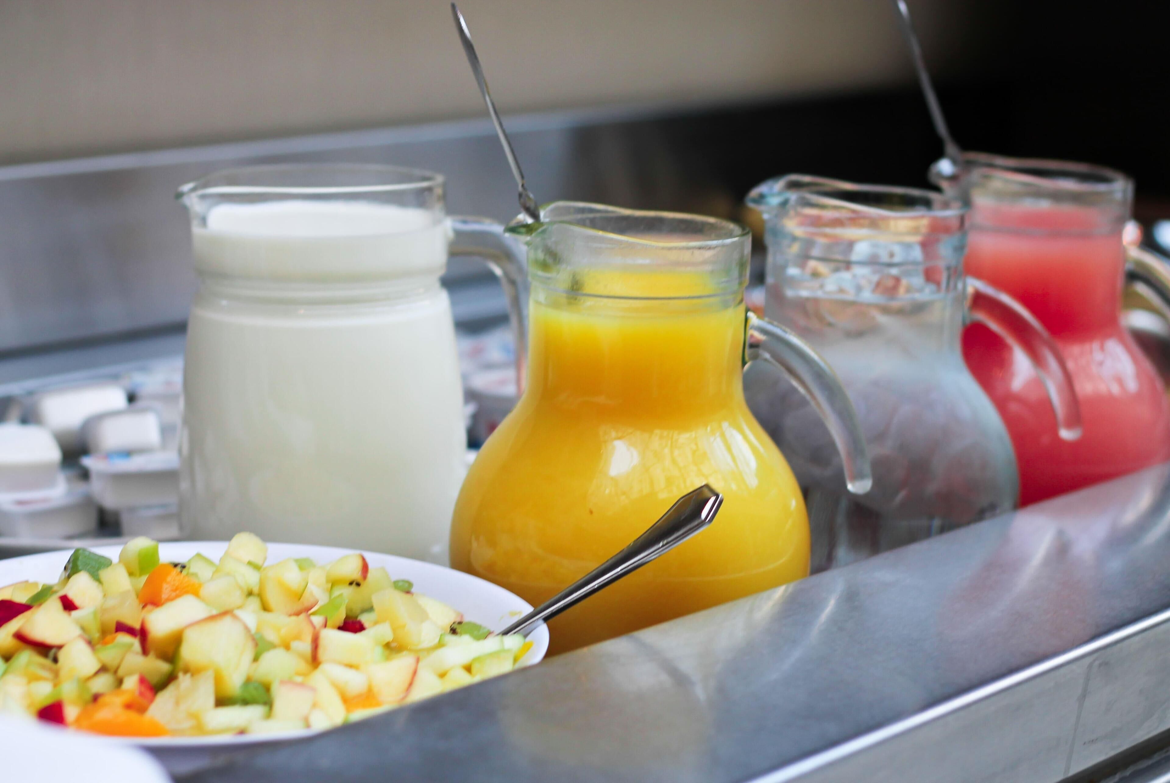 Un bufé de desayuno con una variedad de jugos, una jarras de leche y un plato de ensalada de frutas.