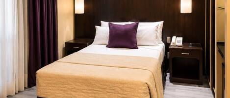 Una habitación de hotel con una cama grande, dos mesitas de noche, un teléfono y una lámpara.