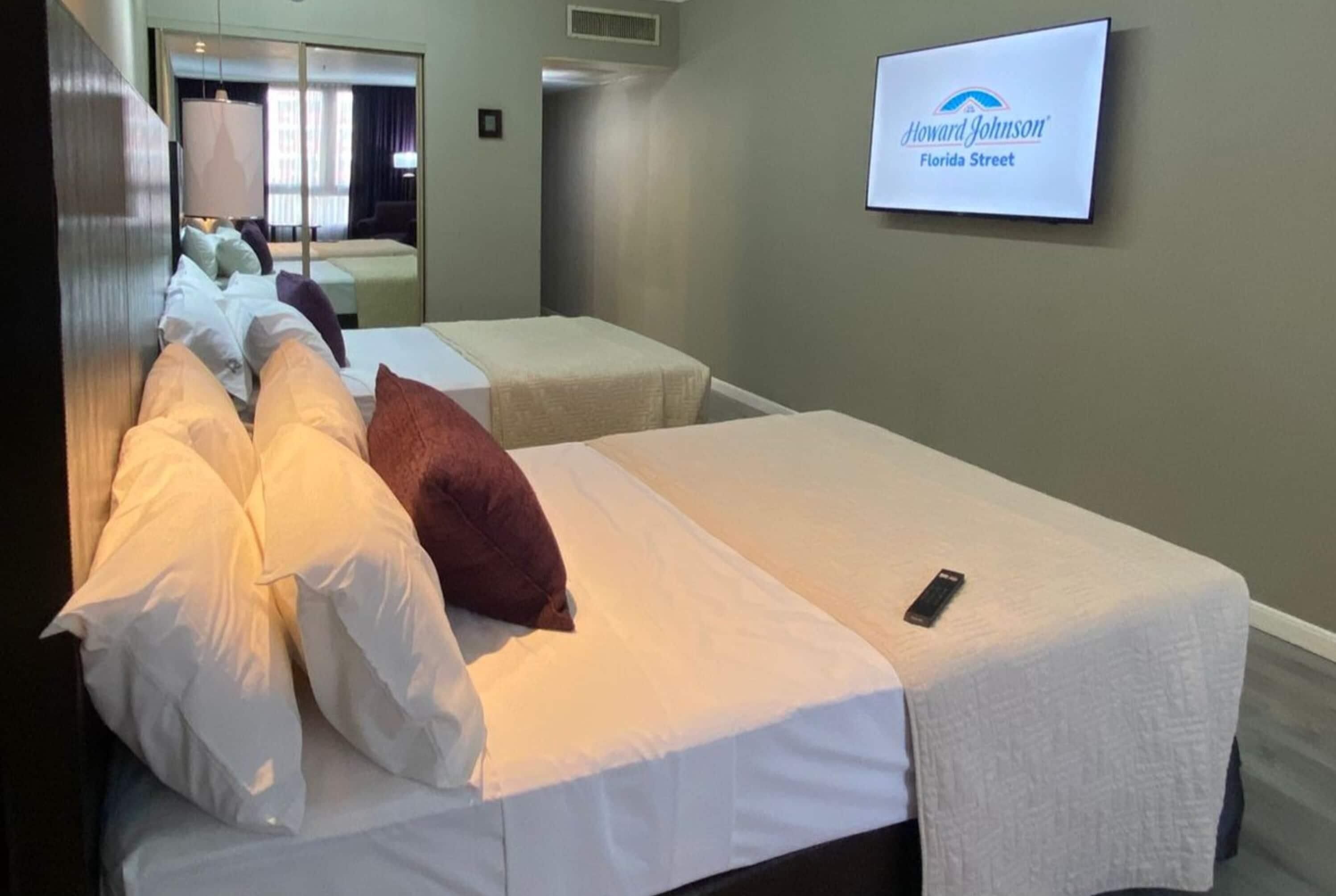 A hotel room with two beds, a TV mounted on the wall, and a sign indicating the hotel name.