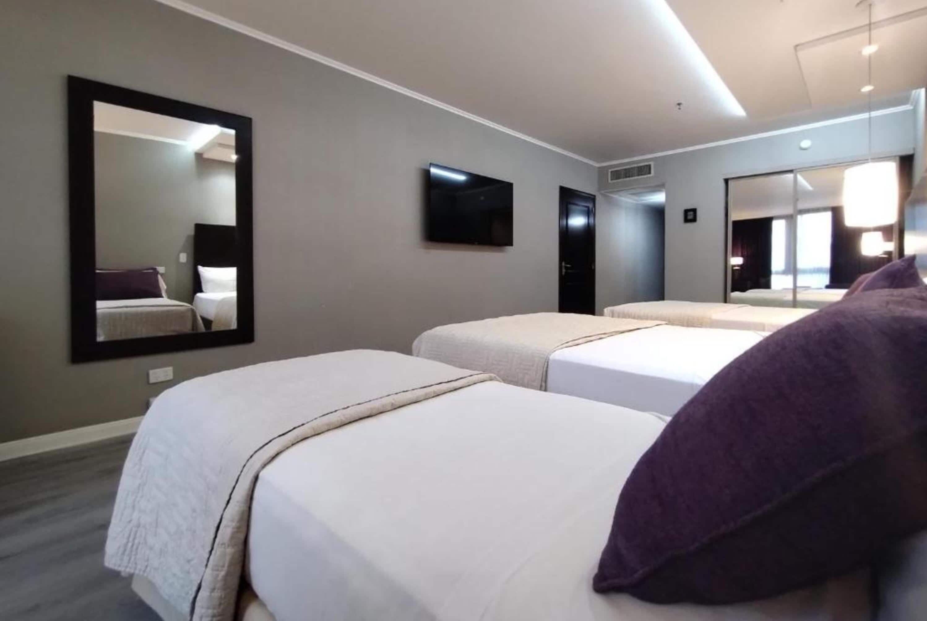 A hotel room with two beds, a large mirror, a flat-screen TV, and a door leading to another room.