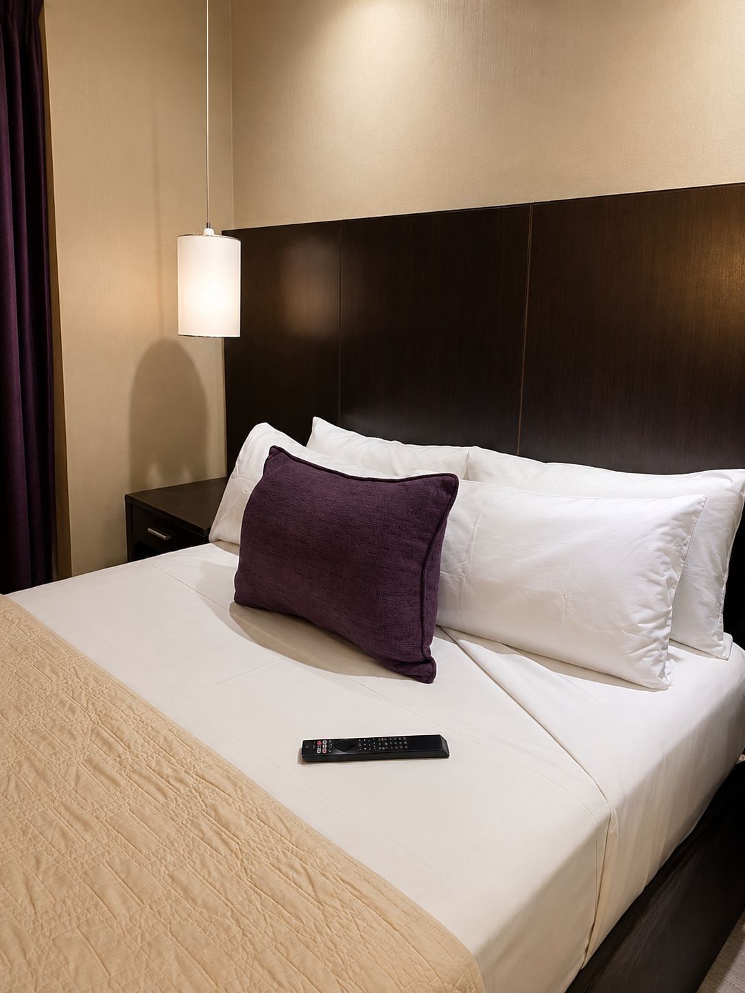 Ein Hotelzimmer mit Bett, Fernbedienung, Nachttisch und Wandlampe.