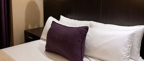 A hotel room with a bed, a remote control, a nightstand, and a wall-mounted lamp.
