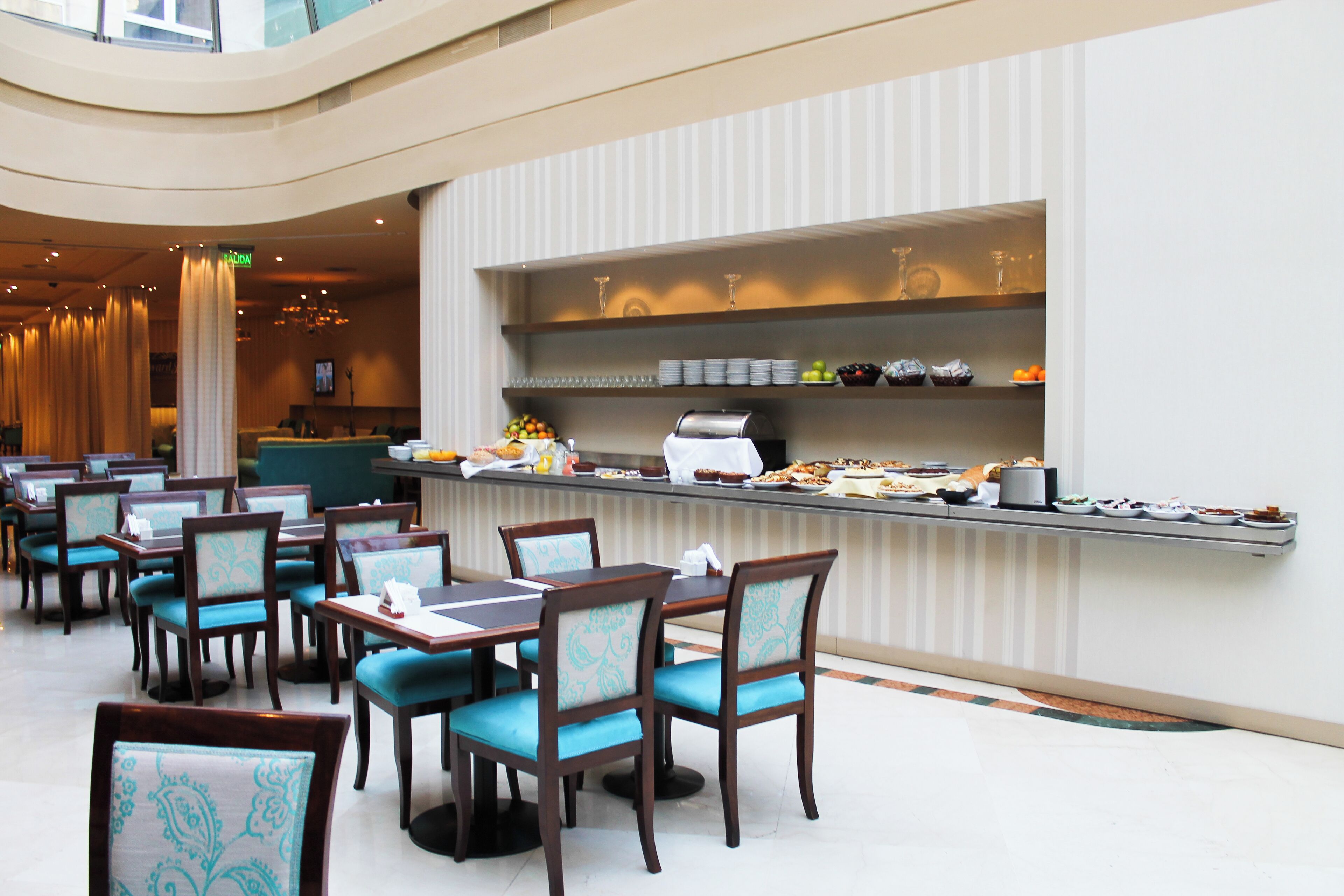 Un espace repas moderne, doté de plusieurs tables et chaises, d’un buffet proposant une variété de plats, et d’un intérieur propre et bien éclairé.
