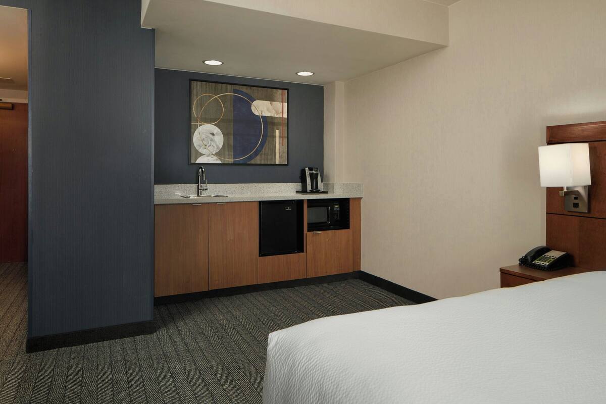 A hotel room with a bed, a small kitchenette with a microwave, a coffee maker, and a telephone.
