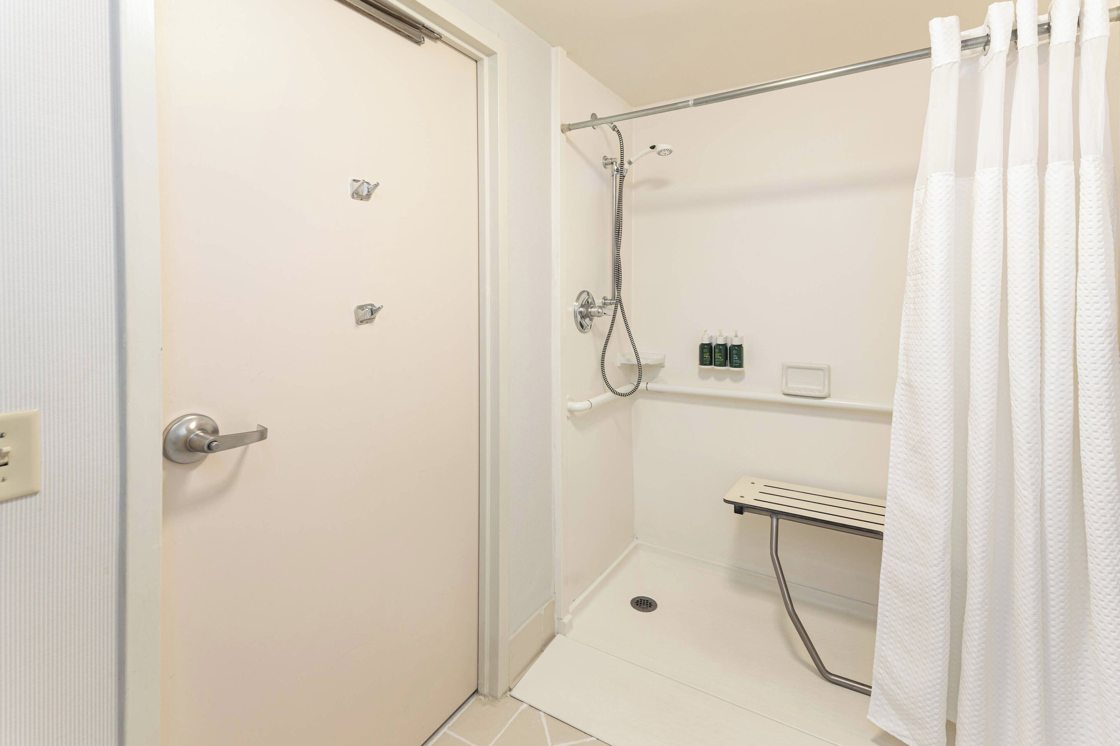 Pequeno espaço de chuveiro branco, fechado por uma porta de vidro, com chuveiro e porta-toalhas.