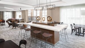 A modern hotel lobby with a central bar area, seating arrangements, and large windows. - Courtyard by Marriott Charlottesville - University Medical Center (Charlottesville)