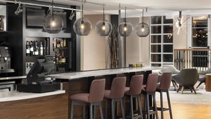 A modern bar area with a long counter, multiple stools, and hanging pendant lights. - Courtyard by Marriott Charlottesville - University Medical Center (Charlottesville)