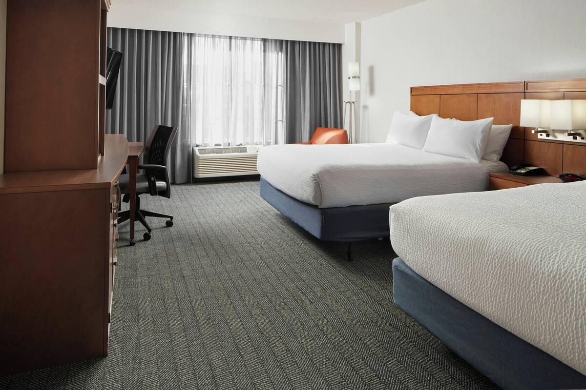 A hotel room with two beds, a desk, a chair, a TV, and a window with curtains.