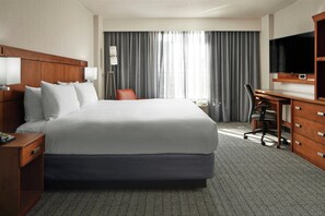 Ein Hotelzimmer mit einem großen Bett, einem Schreibtisch mit Stuhl, einem Fernseher und einem Fenster mit Vorhängen.