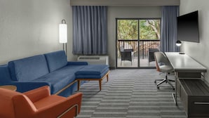 Una habitación de hotel moderna con un sofá azul, un sillón naranja, un escritorio y un televisor.