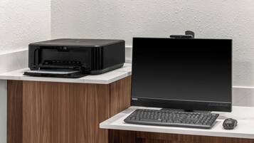 Et moderne kontor med printer, laptop og tastatur på et hvidt skrivebord foran et træskab.