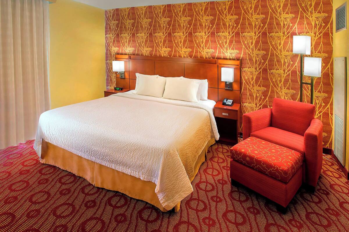 A hotel room with a large bed, a red armchair, and patterned wallpaper.