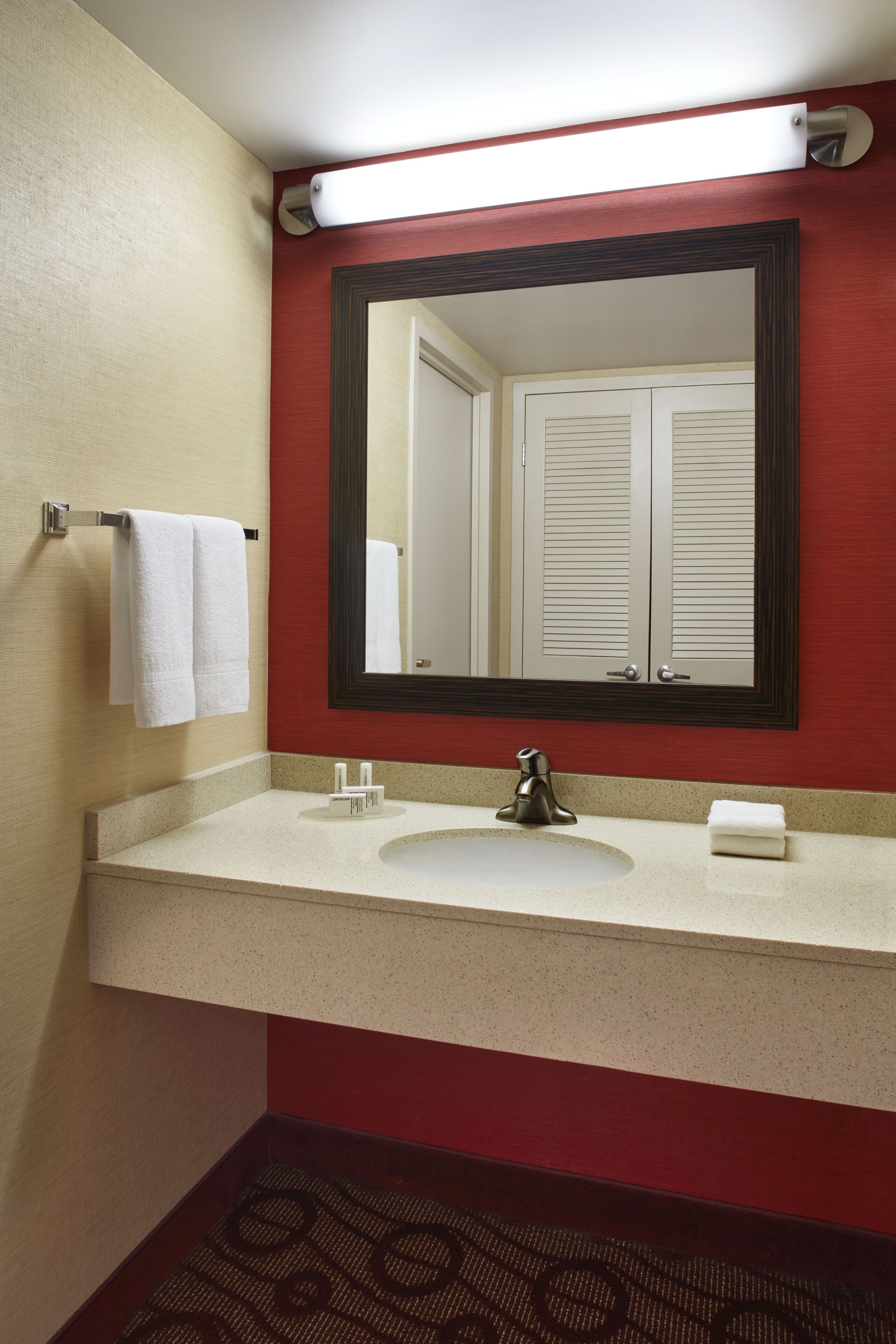 A bathroom with a white sink, a large mirror, and a red wall.