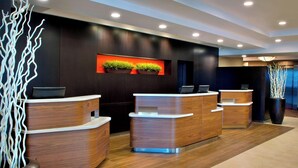 A modern reception area with three wooden reception desks, a dark wall with a red accent, and two potted plants.