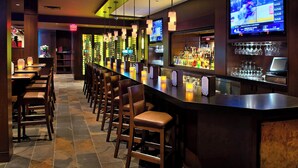 A bar area with a long counter, multiple stools, and a television screen displaying a sports event.