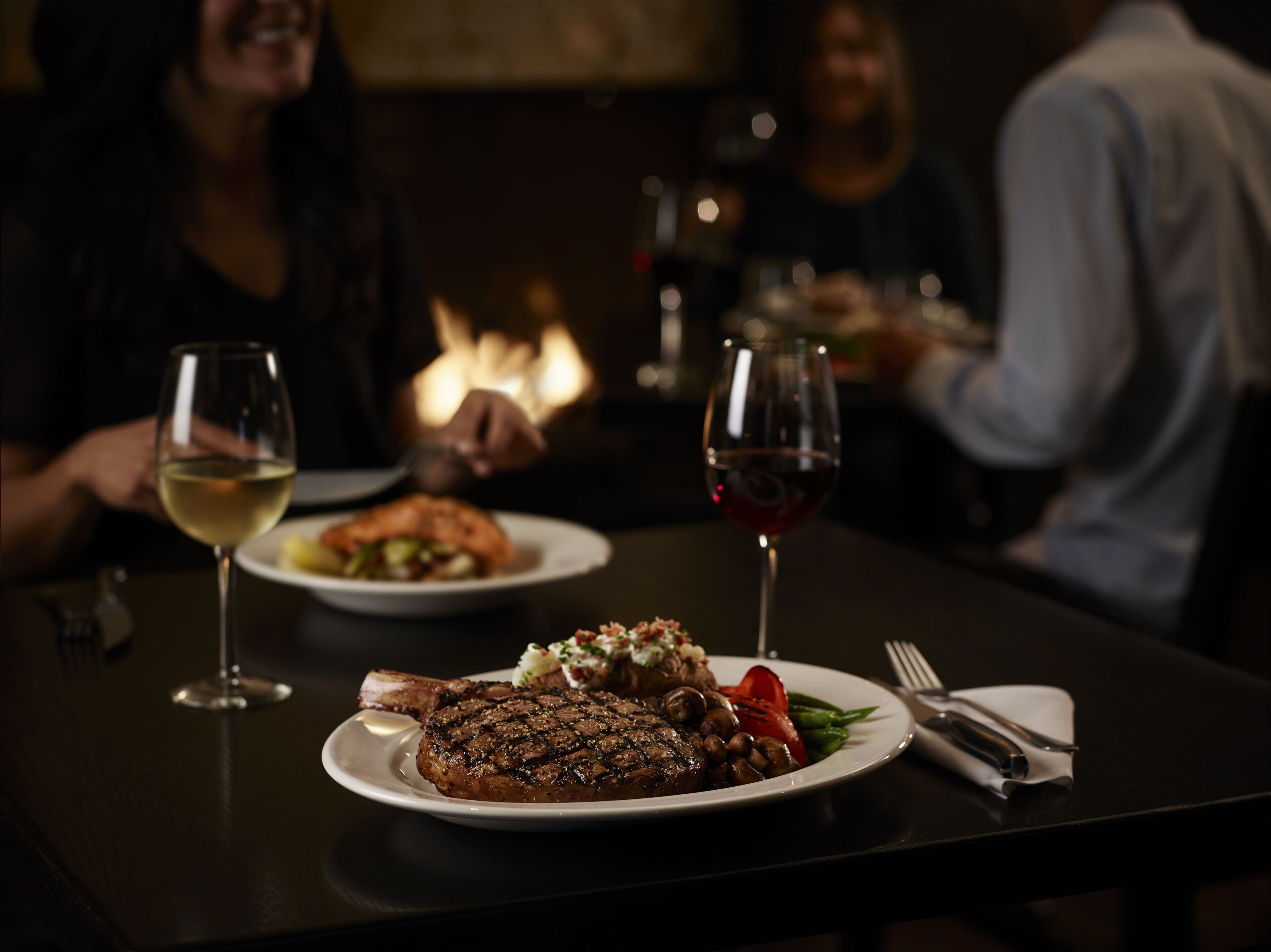 Una mesa de comedor con dos platos de comida, dos copas de vino y una vela encendida.
