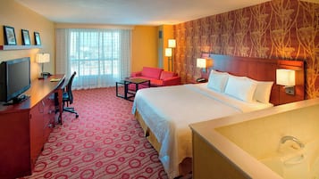A hotel room with a bed, a desk, a chair, a TV, and a bathroom with a bathtub.