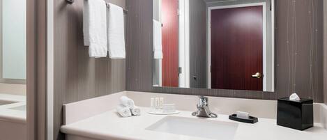 A modern bathroom with a large mirror, white sink, and neatly arranged towels and toiletries.