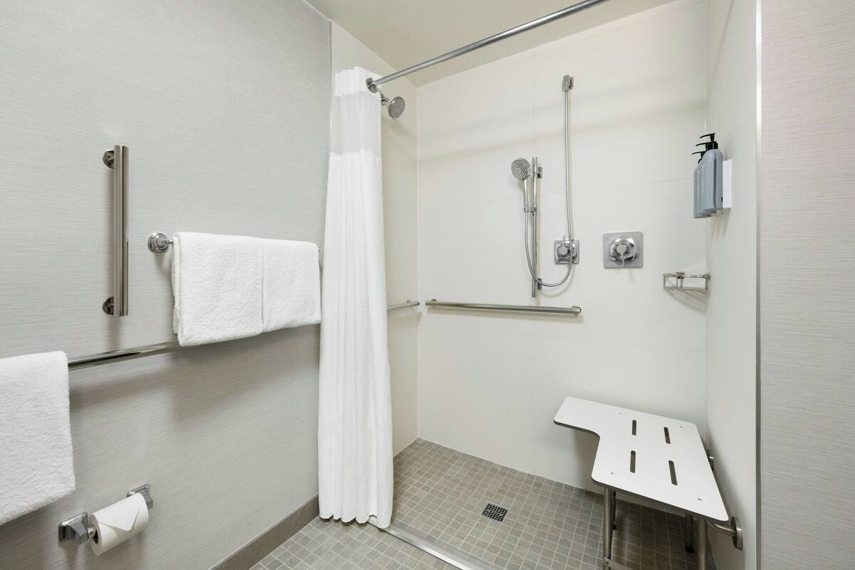 A modern shower area with a glass door, a white towel rack, a showerhead, and a handheld shower attachment.