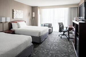 A hotel room with two beds, a desk, a chair, a TV, and a large window with curtains.