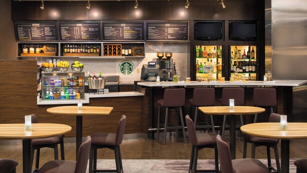 A bar area with multiple seating options, a coffee machine, and a variety of beverages and snacks displayed on shelves. - Courtyard by Marriott Seattle Federal Way (Federal Way)