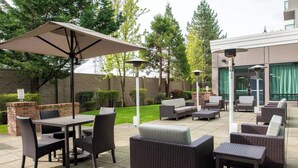 An outdoor patio area with a dining table, chairs, and a large umbrella. - Courtyard by Marriott Seattle Federal Way (Federal Way)