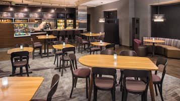 A modern cafe with multiple seating areas, including tables and a sofa, and a bar with a variety of beverages and snacks.